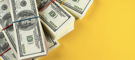 Stacks of hundred-dollar bills on yellow background.