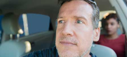 Man driving with passenger in backseat