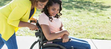 Woman pushing girl in wheelchair outdoors