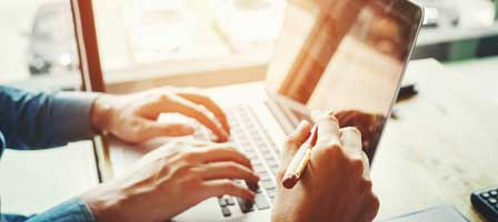 Hands using laptop and holding pen