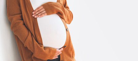 Pregnant woman cradling belly in cardigan