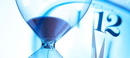 Sand flowing in hourglass, clock in background
