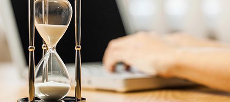 Hourglass beside person typing on laptop