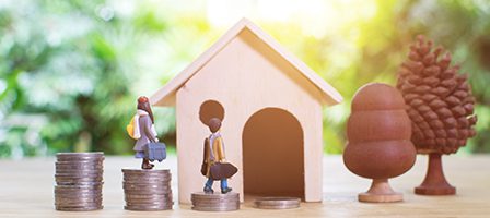 Miniature figures walking towards wooden house model