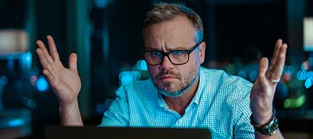 Confused man raising hands at laptop