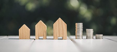 Wooden houses and stacked coins on table