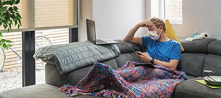 Man in mask reading on couch