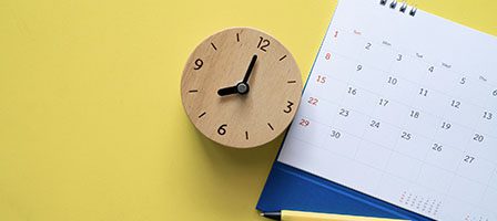 Wooden clock and calendar on yellow background.