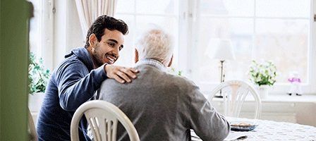 Young man comforting elderly man at table