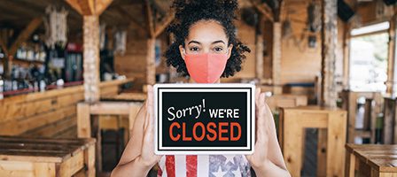 Café closure sign held by masked individual.