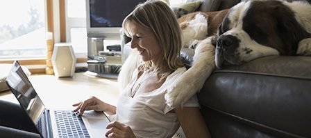 Woman using laptop with sleeping dog nearby.