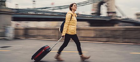 Traveler with suitcase walking by a bridge.