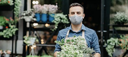 Florist wearing mask holding plants outside shop