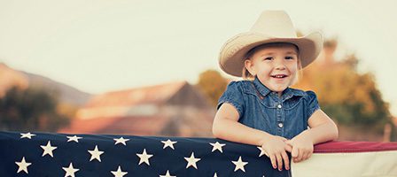 Little girl wearing hat by American flag.