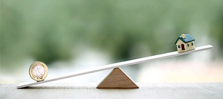 Balancing coin and miniature house on seesaw