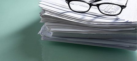 Eyeglasses resting on a pile of papers.