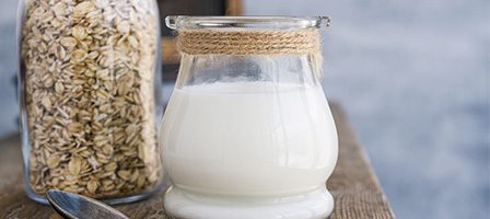Fresh oat milk beside oats jar