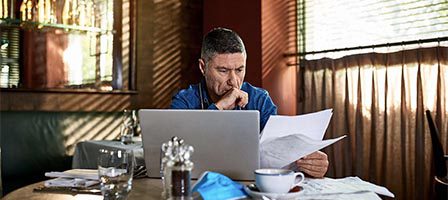 Person concentrating on paperwork with laptop