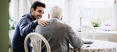 Young man comforting elderly man at table