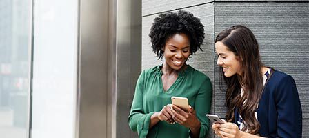 Women sharing smartphone outside office building