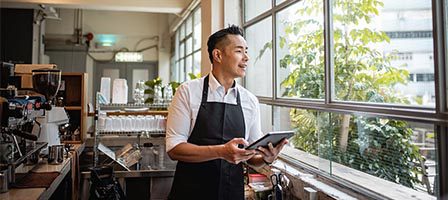 Barista holding tablet near coffee shop window
