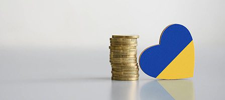 Coins stacked beside a Ukrainian flag heart.