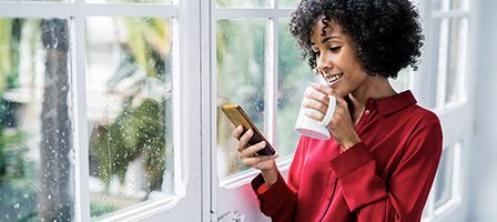 Smiling woman holding phone and coffee