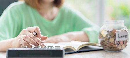 Person budgeting with calculator and coin jar