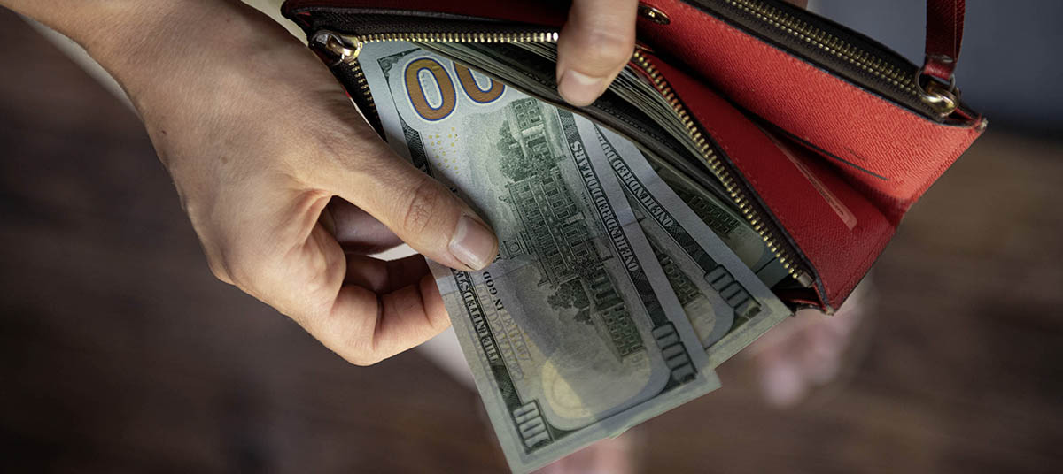 Hand holding hundred-dollar bills over wallet