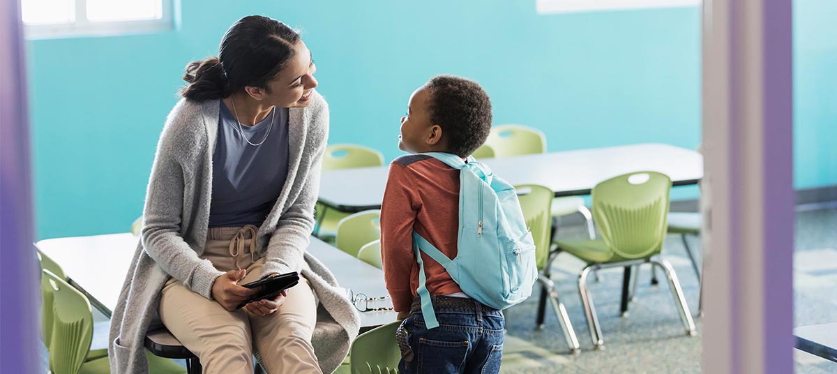 Teacher talking with young student in classroom.