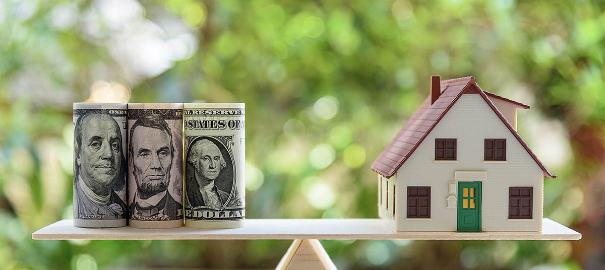Money and house balanced on seesaw