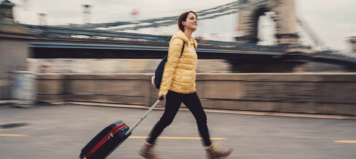 Woman walking with suitcase near bridge