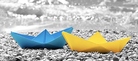 Colorful paper boats on pebbly beach