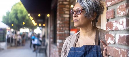 Woman standing outside, wearing glasses and apron