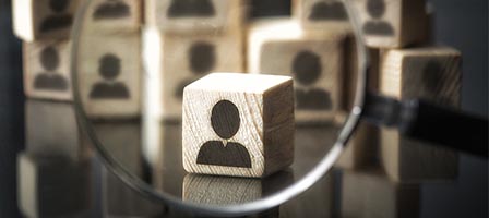 Wooden block with person icon under magnifying glass