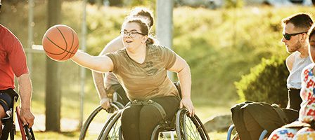 Group playing wheelchair basketball on sunny day.
