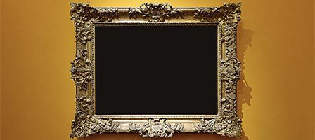Empty ornate picture frame on yellow wall.