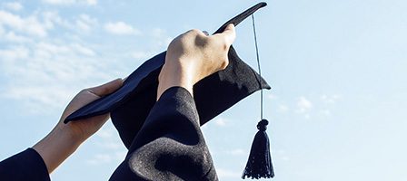 Graduation cap held against blue sky